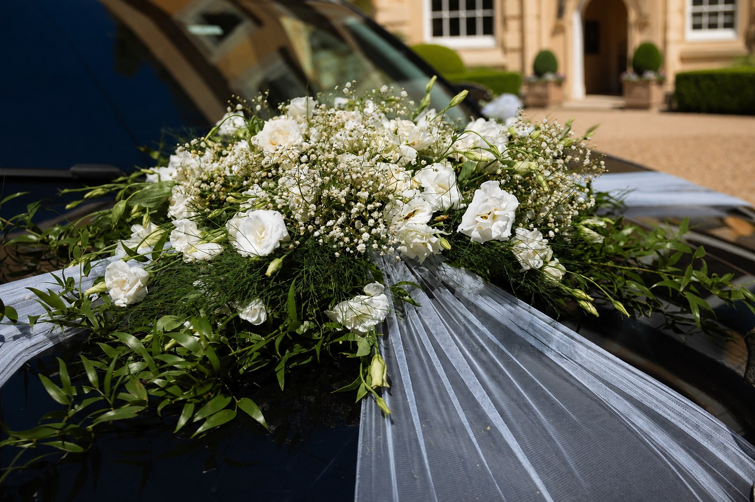 White floral arrangement on a wedding car outside a country house